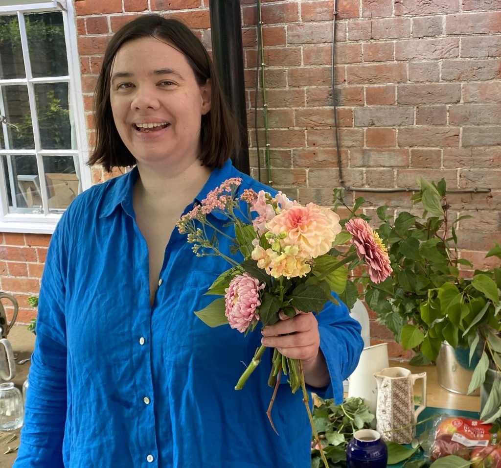 A flower seller smiles as she holds up a bouquet of flowers grown on her allotment
